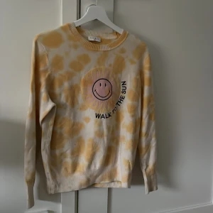 Gul och vit mönstrad tröja från Sandro - Säljer en gul och vit långärmad tröja från Sandro med ett lekfullt mönster och ett stort tryck av en sol med smiley och texten 'WALK TO THE SUN' på bröstet. Perfekt för dig som gillar färg och glada prints! Tie die mönster. Sandro smile