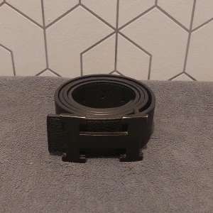 Svart Bälte med H- spänne  - Säljer ett stilrent svart bälte med ett stort H-spänne. || 105 cm långt 