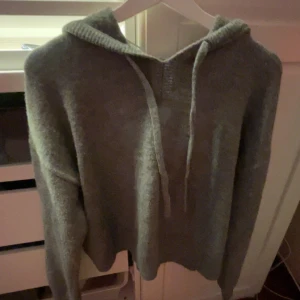 Grå stickad hoodie från Kappahl - Mysig grå stickad hoodie från Kappahl med huva och dragsko. Tröjan har en avslappnad passform och är perfekt för kyliga dagar. Enkel och stilren design som passar till det mesta.