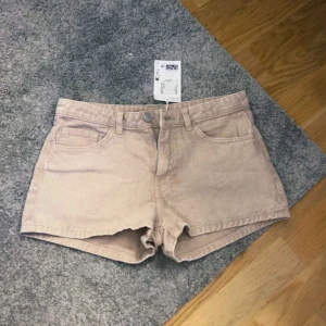 Beiga jeansshorts från Monki - Snygga beiga jeansshorts från Monki med klassisk femficksdesign och bälteshällor. Modellen har normal passform och stängs med dragkedja och knapp. Perfekta för varma dagar och enkla att matcha med olika toppar. Lapp kvar.