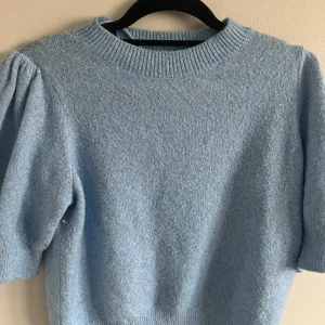 Ljusblå stickad topp från Vero Moda - Superfin ljusblå stickad topp från Vero Moda med kort puffärm och ribbad halsringning. Perfekt för dig som vill ha en mjuk  tröja med lite extra volym på axlarna. Säljes i storlek S. Använd en gång🩷