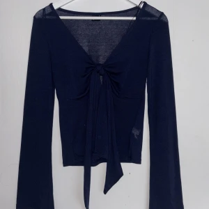 Mörkblå långärmad topp med knyt - Säljer en mörkblå långärmad topp med djup v-ringning och knyt framtill. Tunt, stretchigt material som sitter snyggt på kroppen. Perfekt att styla med jeans eller kjol för en snygg lok. 