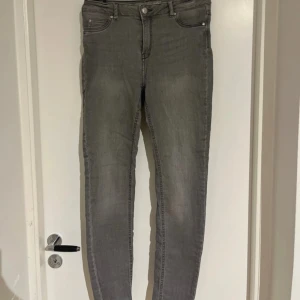 Grå skinny jeans - Säljer ett par grå skinny jeans med klassisk femficksdesign och dragkedja med knapp framtill. Jeansen har en smal passform och är perfekta för en stilren vardagslook.