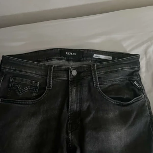 Svarta Replay Anbass jeans - Säljer ett par svarta Replay Anbass jeans som är här snygga detaljer. Jeansen har normal passform och är tillverkade i stretchigt denim för extra komfort. Perfekta för dig som gillar stilrena och tidlösa jeans.