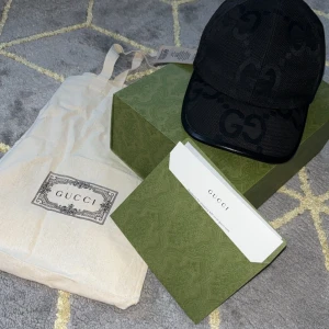 Gucci keps - Snygg svart keps från Gucci med diskret GG-mönster över hela kepsen. Justerbar rem baktill för perfekt passform. Klassisk och stilren design, perfekt för att lyfta din outfit.