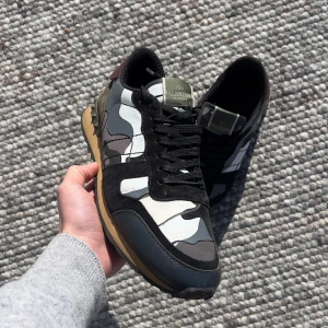 Valentino Rockrunner sneakers med camouflage - Säljer ett par Valentino Rockrunner sneakers med svart, grå och vit camouflage-mönstrad ovandel. Skorna har svarta snören, mockadetaljer och en beige sula med svarta och vinröda inslag vid hälen. Riktigt bra skick utöver lite färg slitnibgar som syns i bild 4. Storlek 42,5 men passar däremot 43 | Priset kan diskuteras vid snabb affär! Skickar inom 24h /Scandi Reventio