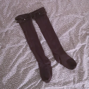 Knästrumpor från Culture strl S/M - Stickade mörkbruna knästrumpor med spetsdetaljer och små silvriga hjärtan på sidorna, går över knäna. Sparsamt använda. Spetsen sticker inte ut när man har dem på sig. Märke Culture strl S/M. 