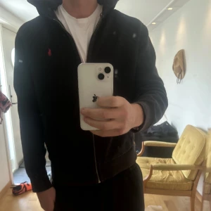 Ralph Lauren hoddie - Säljer en stilren svart hoodie från Ralph Lauren med dragkedja och en liten röd logga på bröstet. Perfekt för en avslappnad look. Den har långa ärmar och en bekväm passform. Storlek L. Otroligt fräscht skick!
