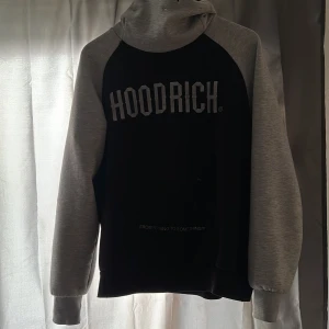Svart och grå hoodie från Hoodrich - Säljer en svart hoodie med grå ärmar och huva från Hoodrich. Stor logga framtill och magficka. Perfekt för en avslappnad stil.