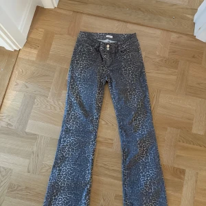 Grå leopardmönstrade jeansbyxor - Säljer ett par  jeansbyxor med leopardmönster. Byxorna har normal passform, utsvängda ben och klassisk femficksdesign med knapp och dragkedja framtill. Passar storlek S och M