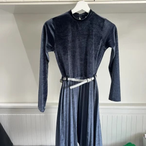 Mörkblå långärmad sammetsklänning med bälte från LC Waikiki - Mörkblå långklänning i mjuk sammet från LC Waikiki. Klänningen har långa ärmar, rund halsringning och ett glittrigt silverfärgat bälte i midjan som ger en snygg detalj. Perfekt för dig som gillar stilrena och bekväma plagg.
