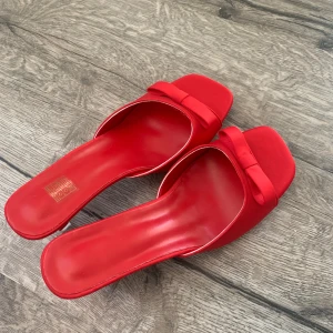 Röda klackade sandaler med rosett - Snygga röda sandaler med öppen tå och liten klack. Skorna har en söt rosettdetalj framtill och en elegant, minimalistisk design. Perfekta för att lyfta vilken outfit som helst med en pop av färg. Aldrig använts