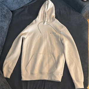 Beige hoodie från McKenzie - Säljer en beige hoodie från McKenzie med logga på bröstet och ryggen. Tröjan har huva med dragsko och en stor magficka framtill. Perfekt för en avslappnad stil och enkel att matcha med det mesta. Den är helt äkta aldrig använts 