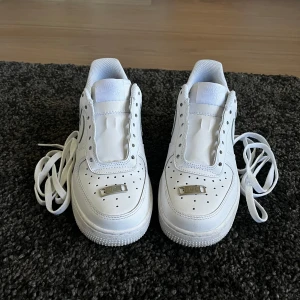 Vita Nike Air Force 1 sneakers -  Helt nya Air force 1 jag har bara använt dem en gång men dem är tyvärr för små för mig storlek 38 så därför säljer jag för jätte bra pris Klassiska helvita Nike Air Force 1 sneakers med rund tå och platt sula. Skorna har snörning och är tillverkade i syntetmaterial med diskret Nike-logga på sidan. Perfekta för en clean och stilren look.
