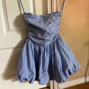 Blå- och vitrandig kortklänning från Stradivarius  - Supersöt blå- och vitrandig kortklänning från Stradivarius teen med ballonglik kjol. Den har inga axelband utan det är banden för att hänga upp den med, alltså syns de inte när man bär den.Klänningen har omlottliknande överdel med öppen rygg och är perfekt för varma dagar. Kolla min profil för fler kläder!