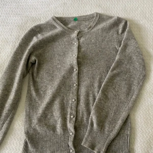 Grå kofta från United Colors of Benetton - Säljer en jättesöt grå kofta med pärlknappar framtill. Skulle säga att den är i storlek XS, har tyvärr klippt bort lappen. 