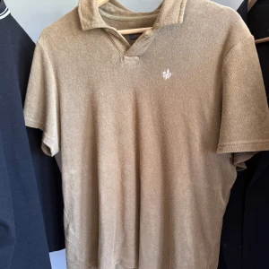 Beige frotté t-shirt från Morris - Säljer en beige t-shirt från Morris i mjuk frotté med klassisk krage och kort ärm. Liten broderad logga framtill. Den är grönare i verkligheten än vad som syns på de första 2 bilderna. 