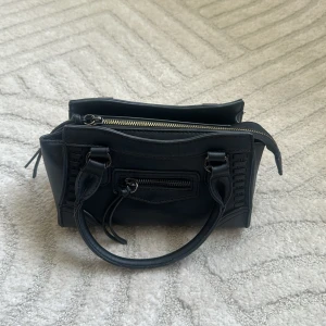 Svart mini handväska med dragkedja - Säljer en svart mini handväska från Ginatricot. Perfekt storlek för det viktigaste och stilren design. Använd några gånger därav lite små defekter på handtagen, kastade tyvärr axelremsbandet som man fick med💖