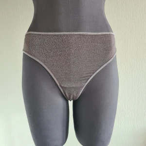 UNDERDEL FRÅN MARLIES DEKKERS  - Oanvänd trosa från MARLIES DEKKERS Manjira Thong Säljer en oanvönd trosa i strl XL.   Thong med grafiska linjer. Linjerna kombineras silverdetaljer för en fin effekt.   Sidorna på denna stringtrosa mäter 4 cm. Den täcker helt skinkorna och den övre delen av höfterna; ljumsken och magen är delvis täckta.  79 % nylon  14 % metalliskt garn  7 % spandex