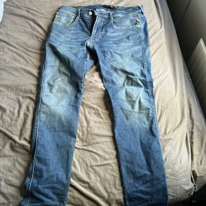 Blå jeans från Replay - Säljer ett par klassiska blå jeans från Replay med dragkedja och knapp framtill. Jeansen har fem fickor och snygga slitningar för en cool look. Perfekta till vardags och passar till det mesta. Modellen är replay anbass och nypris ligger på 1200 kr