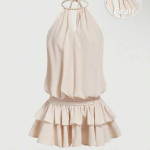 Champagnefärgad halterneckklänning med pärldetaljer - Supersöt kort klänning i champagnefärg med halterneck och volangkjol. Klänningen har pärldetaljer vid halsringningen och i midjan, samt en luftig passform upptill. Helt ny med lappen kvar!!