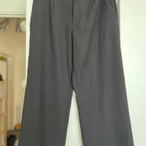 Svarta kostymbyxor med vida ben - Säljer ett par svarta kostymbyxor med klassisk passform och vida ben. Byxorna har pressveck framtill och stängs med dold dragkedja. Perfekta för en stilren look och passar till många olika outfits. Två små fläckar (se bilder) som inte går bort, där av lägre pris. Säljer samma på vinted så kontakta gärna innan ni trycker på ”köp”.