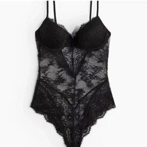 Svart spetsbody med tunna axelband - Säljer en svart body i spets med tunna axelband och vadderade kupor. Bodyn har transparent spetsmaterial och fina spetsdetaljer längs kanterna. Perfekt för att skapa en snygg lager-på-lager-look eller som statement-plagg.