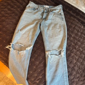 Ljusblå slitna jeans från Zara - Ljusblå jeans från Zara med stora slitningar på båda knäna och bakfickan. Klassisk femficksmodell med knapp och dragkedja. Perfekta för en avslappnad och trendig look.
