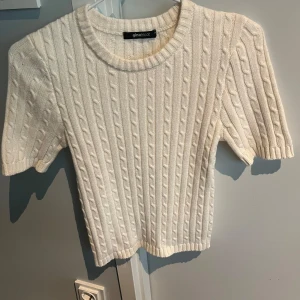Vit kabelstickad topp  - Säljer en söt vit kabelstickad topp från Gina Tricot. Tröjan har korta ärmar, rund halsringning och ett klassiskt kabelstickat mönster. Skriv till mig för ytterligare frågor!😊🫶🩷