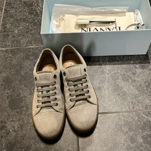 Beige sneakers från Lanvin - Säljer ett par stilrena beige sneakers från Lanvin med ovandel i mocka och platt gummisula. Skorna har snörning framtill och diskret logga på sidan. Perfekta för dig som gillar en clean och klassisk look. pris kan diskuteras vid snabb affär🫵🏽 om ni har några frågor så skriv bara😊