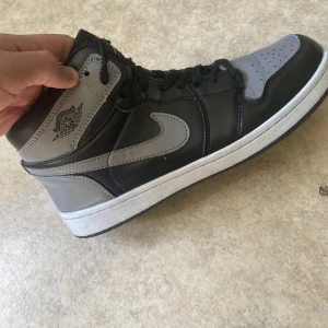 Nike Air Jordan 1 Mid svart och grå - Säljer ett par Nike Air Jordan 1 Mid i svart och grått. Klassisk high-top modell med snörning och vit sula. Perfekta för dig som gillar streetwear och vill ha en ikonisk sneaker i garderoben.