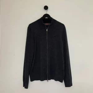 Morris Zipup - Säljer en mörkgrå kofta från Morris i 100% merinoull. Tröjan har dragkedja framtill, lång ärm och en diskret broderad logga på bröstet. Perfekt för lager-på-lager och stilren look. Storlek M men passar S 