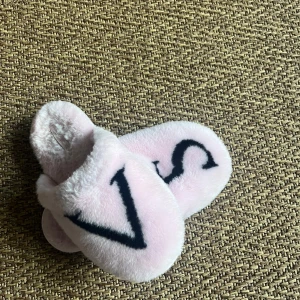 Rosa fluffiga tofflor från Victoria's Secret - Supermjuka och fluffiga tofflor i ljusrosa från Victoria's Secret med stora svarta bokstäver 'VS' på ovansidan. Perfekta att mysa runt i hemma, med öppen häl och rund tå för extra komfort. Storleken är Onesize!!!!!