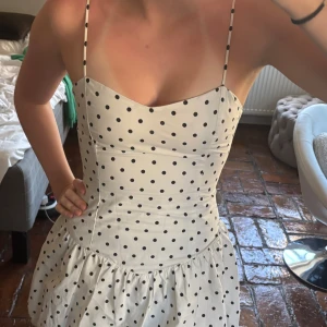 Vit prickig kortklänning med smala axelband - Supersöt vit kortklänning med svarta prickar och smala axelband. Klänningen har en figurnära passform upptill och en volangliknande kjol. Perfekt för sommaren!                                        Säljer pga är för liten för mig💗                                            Prislappen sitter kvar!!💗