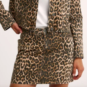 Leopardmönstrad jeanskjol - Säljer en cool leopardmönstrad jeanskjol med klassisk femficksdesign och bälteshällor. Kjolen har en rak passform och är i kort modell. Stor i storlek, passar 36-40.