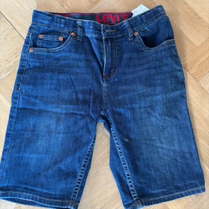 Levi's jeansshorts 511 - Snygga blå jeansshorts från Levi's modell 511. Klassisk femficksdesign med knapp och dragkedja i gylfen. Shorts i normal passform med tydliga röda Levi's-detaljer i midjan och bakficka. Perfekta för varma dagar.
