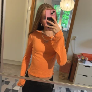 Orange ribbad långärmad topp med fjäril - Säljer en orange ribbad långärmad topp med broderad fjäril-cutout framtill. Tröjan har utsvängda ärmar och croppad passform. Perfekt för dig som vill ha en färgglad och trendig look.🩷
