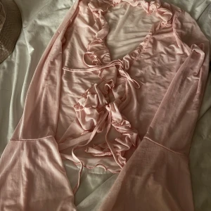 Ljusrosa volangtopp med knyt - Säljer en favorit ljusrosa topp med volangdetaljer och knyt framtill. Väldigt feminin och vacker, Toppen har långa ärmar och är tillverkad i ett tunt, mjukt material.