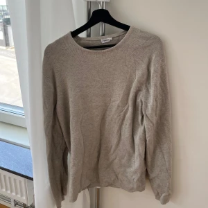 Beige stickad tröja från Filippa K - Säljer en stilren beige stickad tröja från Filippa K. Tröjan har rund halsringning och långa ärmar. Perfekt för lager-på-lager och passar till många olika outfits.