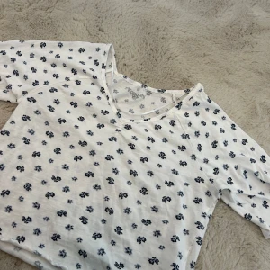 Vit blommig topp från Kappahl - Säljer en söt vit topp från Kappahl i storlek XS med små blå blommor över hela tyget. Toppen har korta ärmar och en rund halsringning. Perfekt för en avslappnad och somrig stil! 🩷 Köparen står för frakt och priset går alltid att diskutera🩷