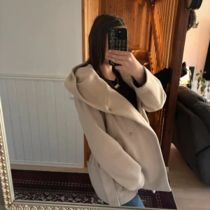 Kappa med luva - Säljer beige kappa med luva från amisu, den är använd ich der syns vid armarna som är noppriga men annars är den perfekt för våren/hösten
