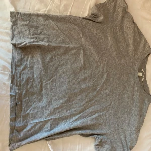 Grå basic t-shirt från H&M - Enkel grå t-shirt från H&M i mjuk bomull. Klassisk passform med rund halsringning och korta ärmar. Perfekt till vardags och lätt att matcha med andra plagg.