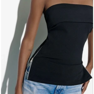 Svart tubtopp med dragkedja från Zara - Säljer en svart axelbandslös tubtopp från Zara med coola dragkedjor längs sidorna. Toppen har en bandeauformad överdel och är figurnära med en lätt utsvängd nederdel.