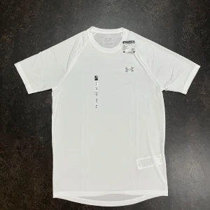  t-shirt Under Armour stl S - Snygg vit t-shirt från Under Armour med diskret logga på bröstet. Tillverkad i ett lätt och snabbtorkande syntetmaterial som passar perfekt för träning. Klassisk passform med korta ärmar och rund hals. Enkel och clean design som funkar till alla sportiga outfits.