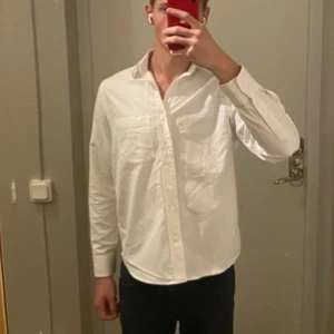 Vit skjorta  - Vit skjorta från H&M Essentials, regular fit med lång ärm och bröstficka. Skjortan är gjord av bomull och har knappar framtill och vid ärmslut.