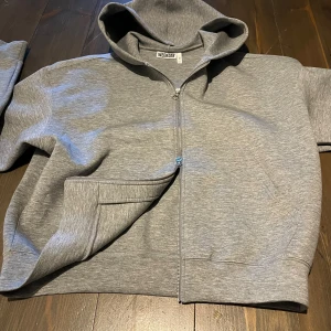 Grå hoodie med dragkedja från Weekday - Säljer en stilren grå hoodie från Weekday i storlek M. Tröjan har tvådragkedjor, huva och två stora fickor framtill. Materialet är mjuk bomullsmix som är skönt mot huden. Perfekt för chill dagar eller när du vill ha en enkel look. köpt ny för 600kr