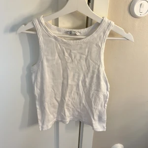 Vit ribbad linnetopp i bomull - Säljer en enkel och fräsch vit ribbad linnetopp från Cubus i ekologisk bomull. Toppen är ärmlös med rund halsringning och har en tight passform som sitter snyggt till jeans eller kjol. Perfekt för varma dagar eller som lager under skjorta.