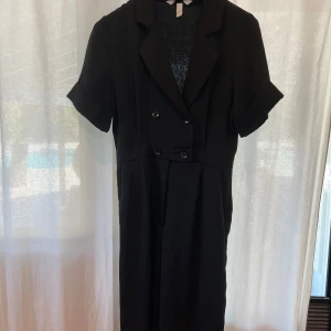 Svart jumpsuit med knappar - Stilren svart jumpsuit från H&M med korta ärmar och dubbelknäppning framtill. Jumpsuiten har klassisk krage och kavajliknande slag, vilket ger en cool och dressad look. Perfekt för dig som gillar minimalistisk stil och vill sticka ut med enkla detaljer ❤️‍🔥