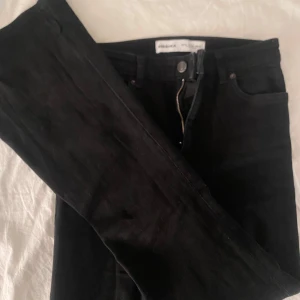 Svarta utsvängda jeans från Bershka - Svarta but cut jeans från Bershka i storlek 36. Klassisk femficksmodell med dragkedja och knapp framtill. Snygg passform. Perfekta till sneakers.