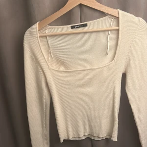 Ribbad vit långärmad topp Gina Tricot - Ribbad långärmad topp från Gina Tricot i mjuk vit färg. Toppen har fyrkantig urringning och en liten slits vid ärmslutet för en extra detalj. Perfekt att styla med jeans eller kjol för en clean look. Tröjan är aldrig använd då den inte passat i storleken 